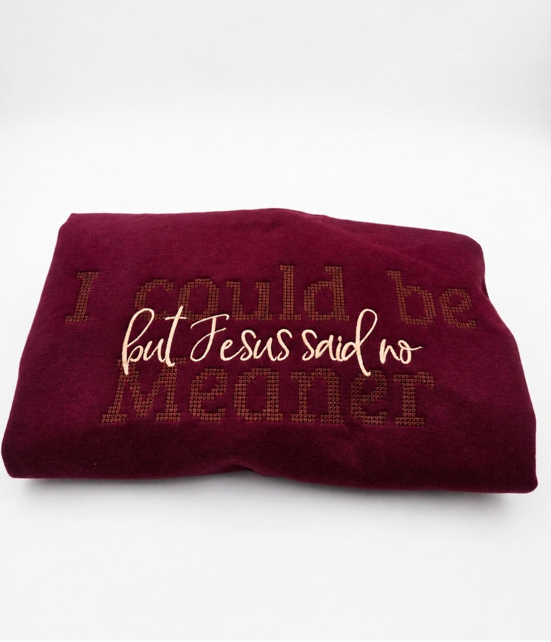 A folded burgundy fleece blanket featuring the embroidered text 'I could be meaner but Jesus said no' in cream and brown tones, set against a plain white background.